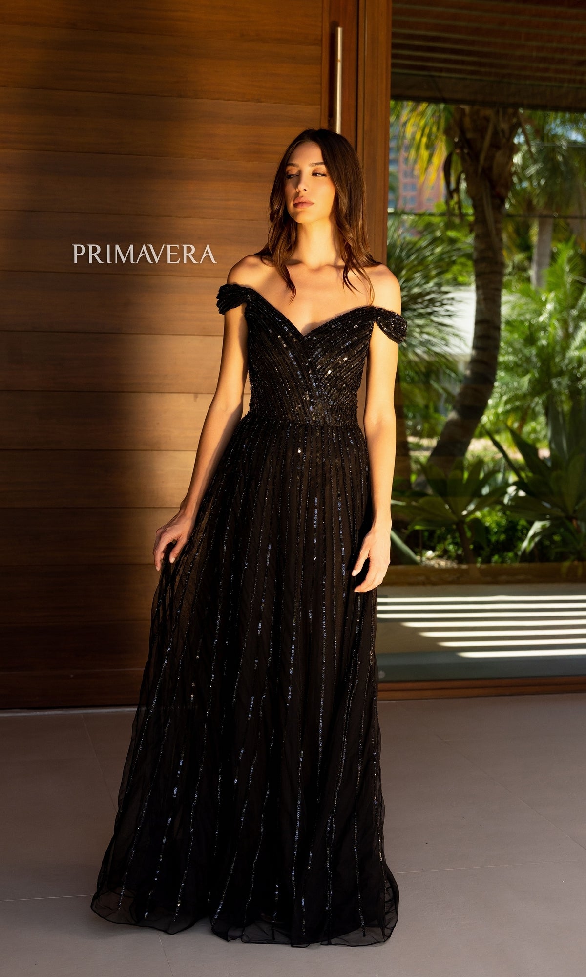 A woman in a black Long Prom Dress 13125 by Primavera with sequins stands before a wooden wall featuring the